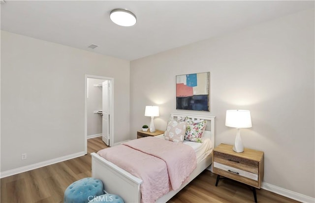 bedroom featuring a walk in closet, visible vents, baseboards, and wood finished floors