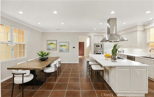 kitchen featuring arched walkways, island range hood, dark tile patterned flooring, appliances with stainless steel finishes, and a center island