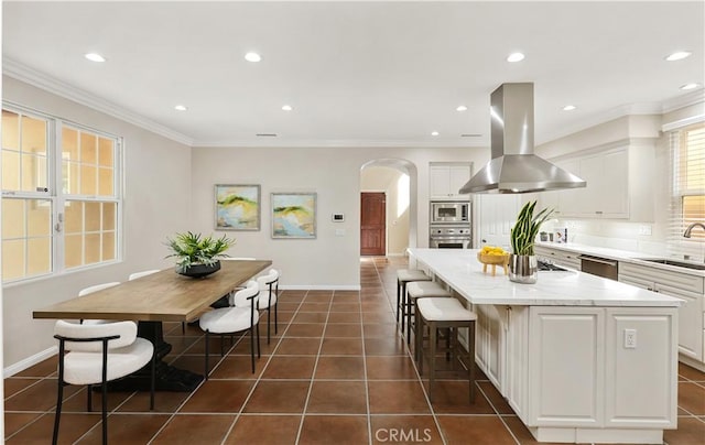 kitchen with island exhaust hood, appliances with stainless steel finishes, a kitchen island, a sink, and arched walkways