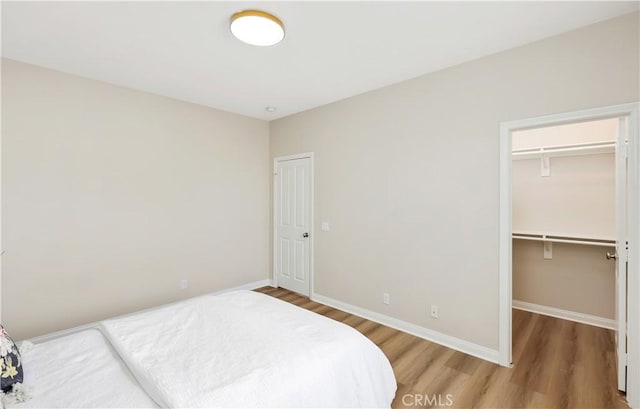 bedroom featuring a closet, a spacious closet, baseboards, and wood finished floors