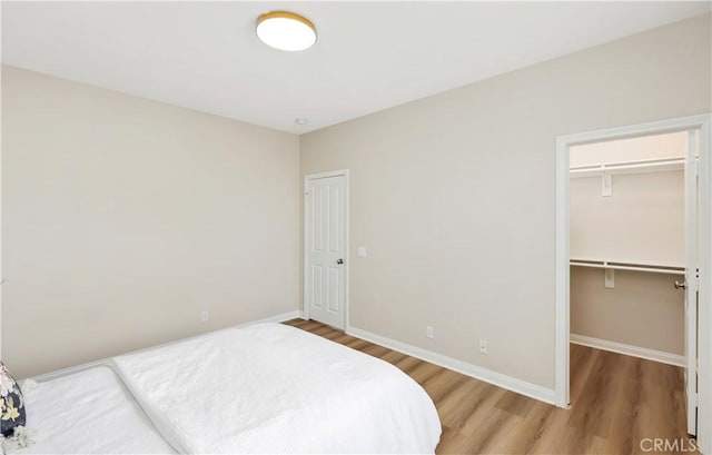 bedroom with wood finished floors, baseboards, a walk in closet, and a closet