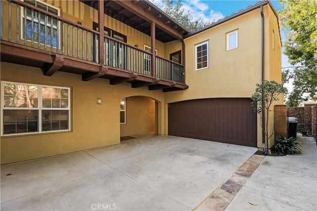 rear view of house featuring a balcony, a garage, stucco siding, and concrete driveway