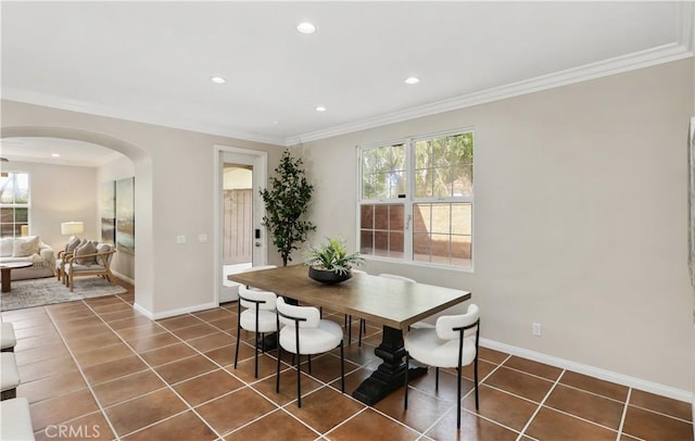 dining space with dark tile patterned floors, arched walkways, and crown molding