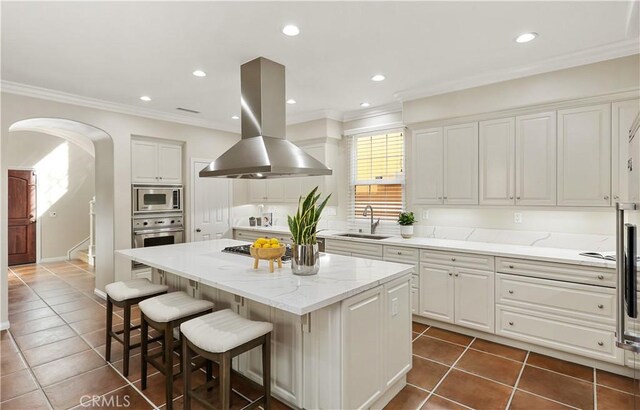kitchen featuring stainless steel appliances, a sink, island range hood, dark tile patterned flooring, and ornamental molding