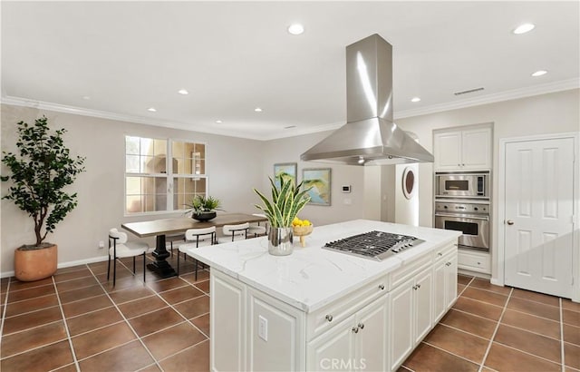 kitchen with island range hood, appliances with stainless steel finishes, ornamental molding, and dark tile patterned flooring