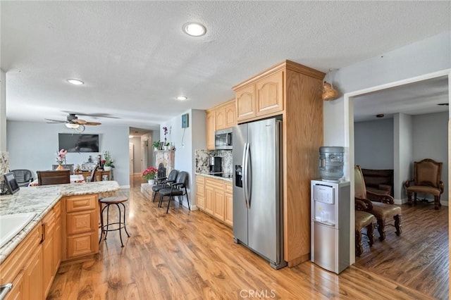 kitchen with stainless steel appliances, light brown cabinetry, light wood-style floors, ceiling fan, and a kitchen breakfast bar