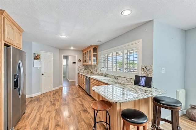 kitchen with a peninsula, a sink, appliances with stainless steel finishes, radiator, and glass insert cabinets