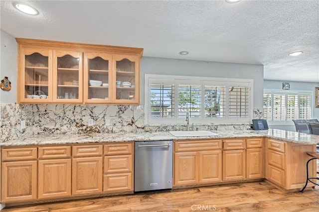 kitchen with a sink, a peninsula, stainless steel dishwasher, and light stone countertops