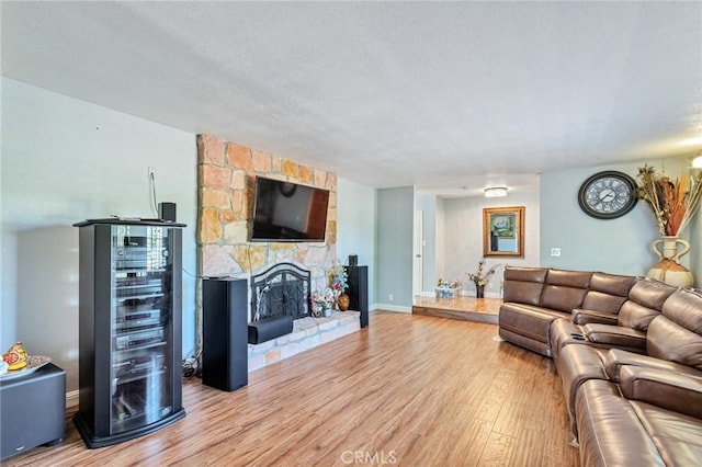 living room with wine cooler, baseboards, wood finished floors, and a stone fireplace