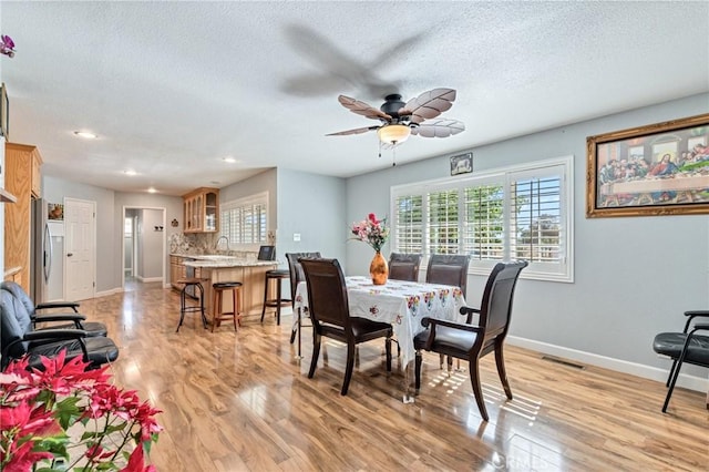 dining room featuring visible vents, light wood-style floors, ceiling fan, a textured ceiling, and baseboards