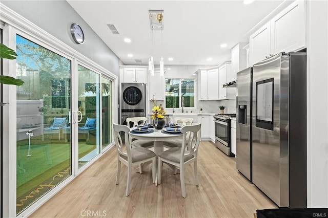 kitchen with appliances with stainless steel finishes, stacked washer / drying machine, white cabinetry, and light wood-style flooring