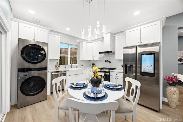 kitchen with stainless steel appliances, a sink, stacked washer / drying machine, light countertops, and wall chimney range hood