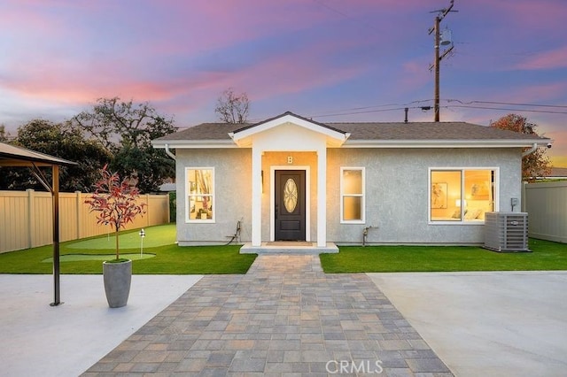 view of front facade with a patio, central AC unit, fence, a yard, and stucco siding