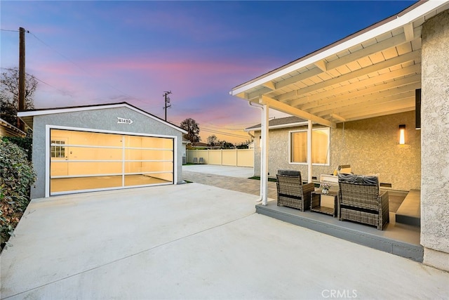 patio terrace at dusk featuring an outbuilding, a detached garage, and fence