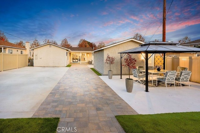 back of house at dusk featuring a patio, fence, outdoor dining area, a gazebo, and stucco siding