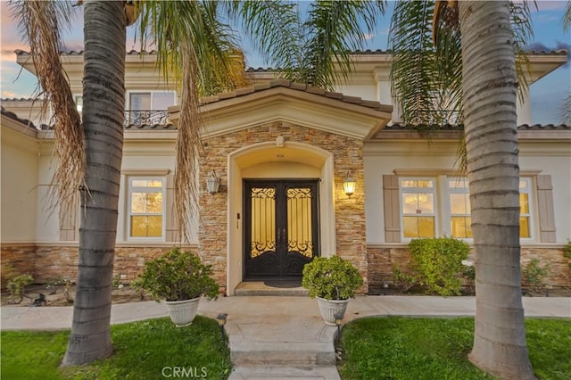 doorway to property featuring stucco siding, stone siding, and french doors