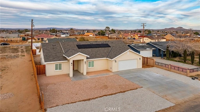 ranch-style home with stucco siding, roof mounted solar panels, fence, a garage, and a residential view