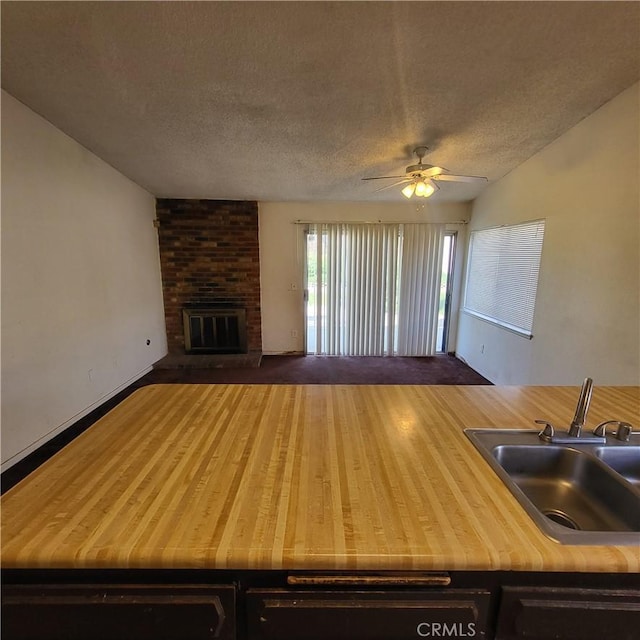 interior space featuring a textured ceiling, ceiling fan, a fireplace, wood finished floors, and a sink