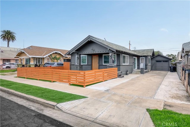 bungalow with a garage, concrete driveway, a fenced front yard, and an outdoor structure