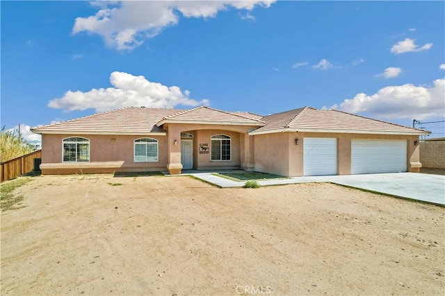 mediterranean / spanish-style home featuring a tiled roof, an attached garage, fence, and driveway