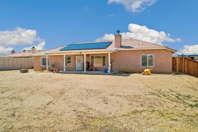 back of house featuring a patio, solar panels, a fenced backyard, stucco siding, and a chimney