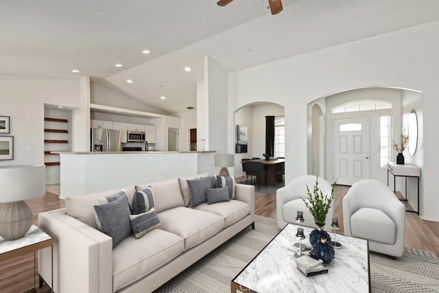 living room with arched walkways, plenty of natural light, light wood-style flooring, and lofted ceiling