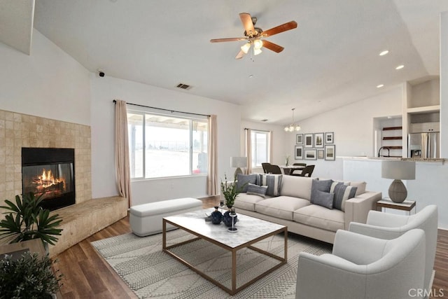 living room with visible vents, vaulted ceiling, ceiling fan with notable chandelier, a tile fireplace, and wood finished floors