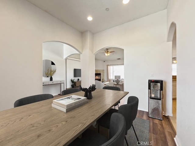 dining space with ceiling fan, dark wood-style floors, arched walkways, and a tile fireplace