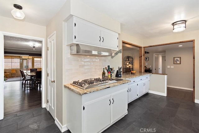 kitchen featuring baseboards, decorative backsplash, stainless steel gas cooktop, under cabinet range hood, and white cabinetry