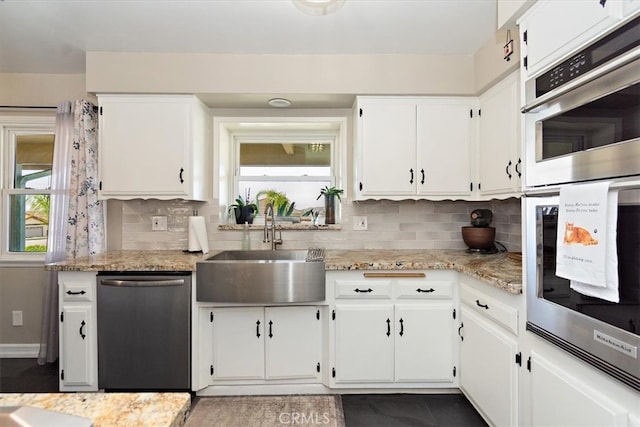 kitchen featuring light stone countertops, stainless steel appliances, a sink, white cabinets, and decorative backsplash