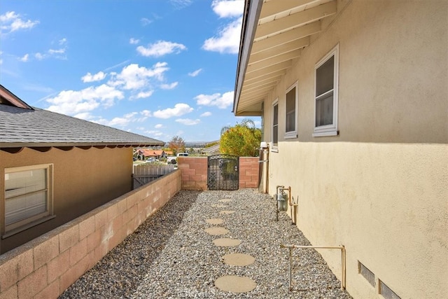 view of home's exterior featuring a shingled roof, a gate, fence, and stucco siding