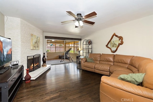 living area with ceiling fan, a brick fireplace, and wood finished floors