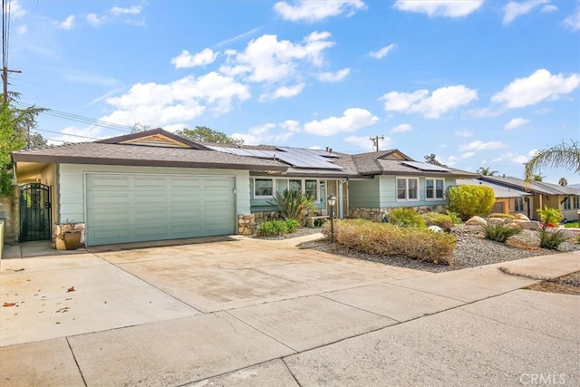 ranch-style house featuring an attached garage, stone siding, driveway, and solar panels