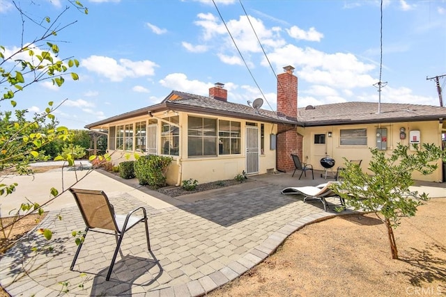 back of house with a patio, a chimney, a sunroom, and stucco siding