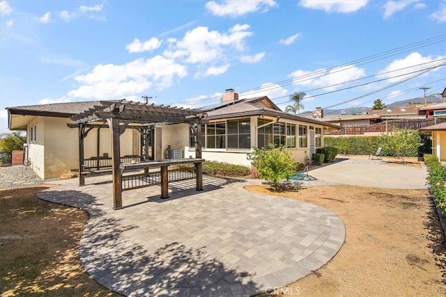 rear view of house with stucco siding, a sunroom, a patio area, fence, and a pergola