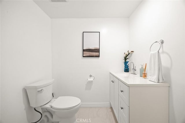 half bathroom featuring marble finish floor, vanity, toilet, and baseboards