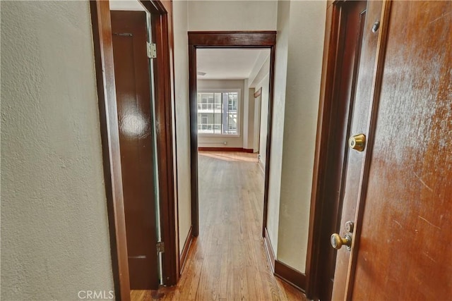 hallway featuring a textured wall, wood finished floors, and baseboards