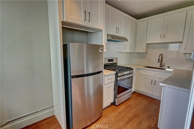 kitchen with stainless steel appliances, light wood-style flooring, white cabinetry, a sink, and under cabinet range hood