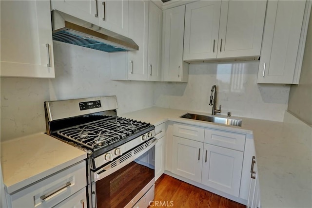 kitchen with stainless steel gas range oven, white cabinets, wood finished floors, under cabinet range hood, and a sink