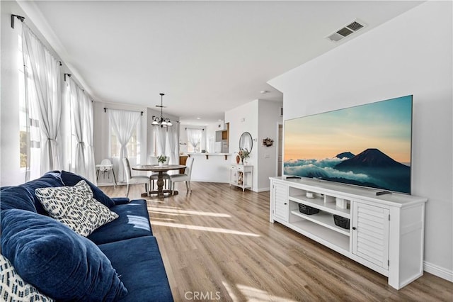 living area with baseboards, wood finished floors, visible vents, and an inviting chandelier