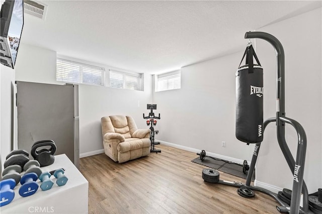 exercise room with wood finished floors, visible vents, and baseboards