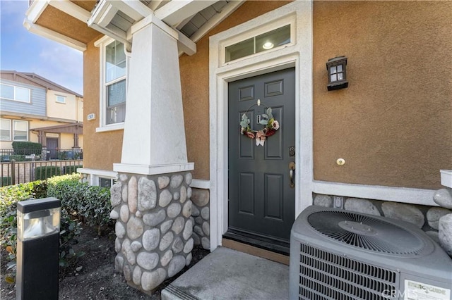 entrance to property with central AC, fence, and stucco siding