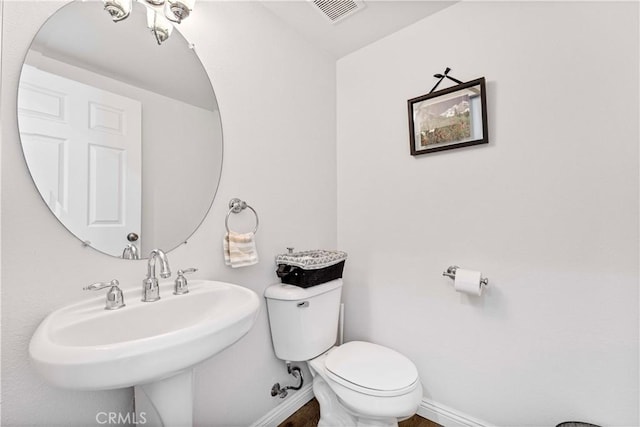 half bath with toilet, baseboards, visible vents, and a sink