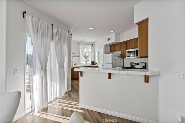 kitchen featuring brown cabinets, stainless steel appliances, tile counters, a peninsula, and a kitchen breakfast bar