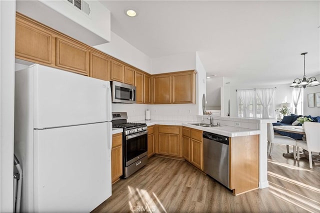 kitchen with light wood finished floors, appliances with stainless steel finishes, a peninsula, light countertops, and a sink