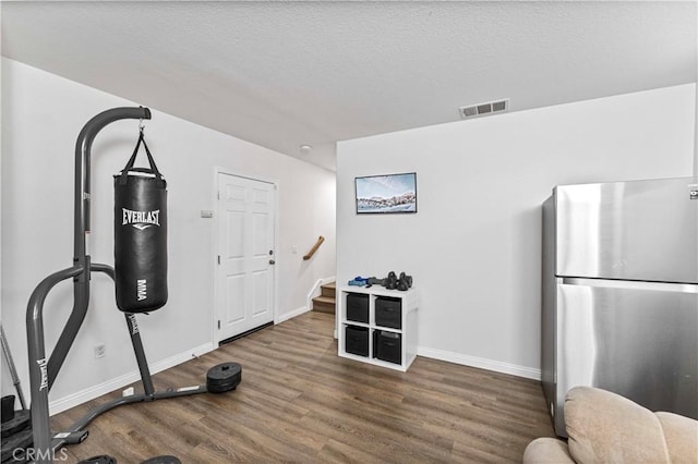 workout area featuring a textured ceiling, wood finished floors, visible vents, and baseboards