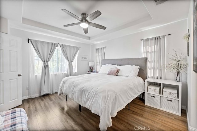 bedroom featuring a tray ceiling, visible vents, ceiling fan, and wood finished floors