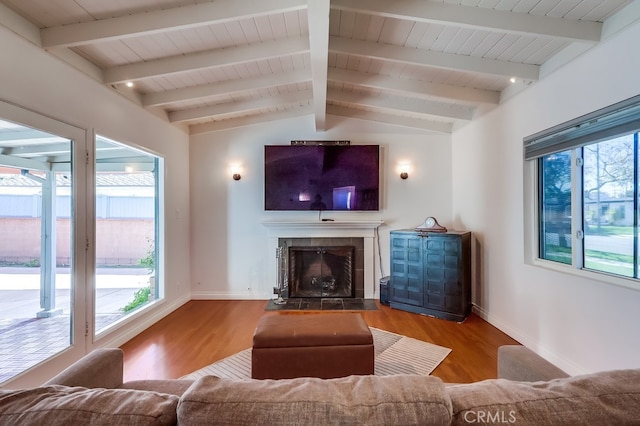 living area featuring vaulted ceiling with beams, plenty of natural light, a tiled fireplace, and wood finished floors