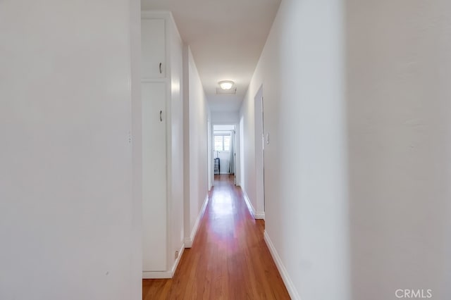 corridor featuring light wood-style flooring and baseboards