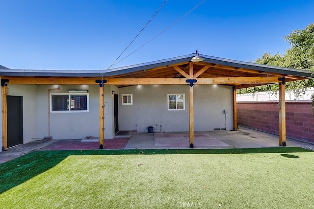 rear view of property featuring a yard, a patio area, fence, and stucco siding